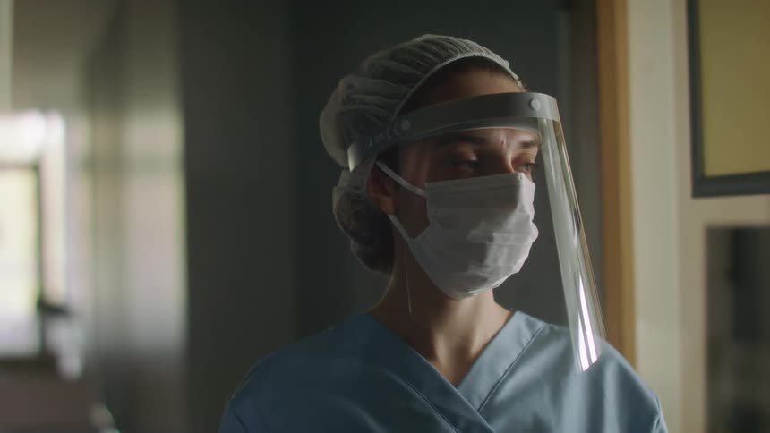A female nurse wearing a face mask and plastic face shield