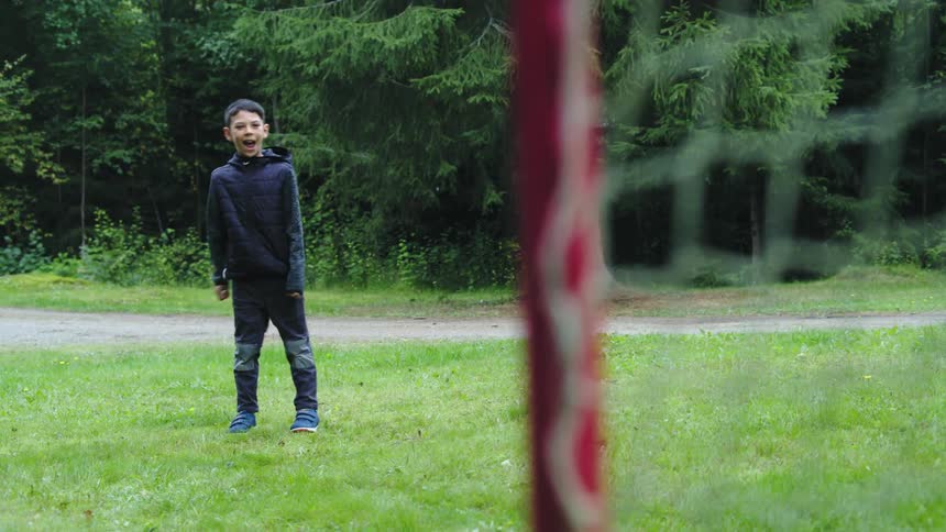 A boy kicks a soccer ball into the goal and cheers