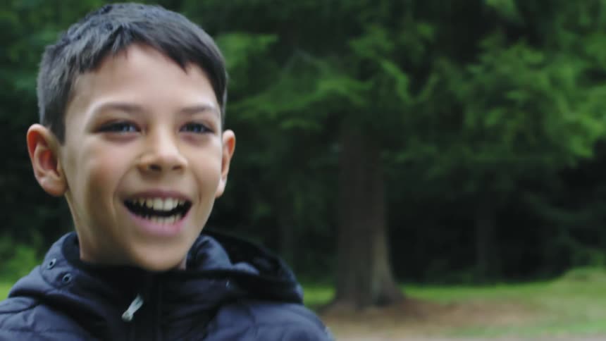 A boy is standing still looking ahead and then he throws something and smiles
