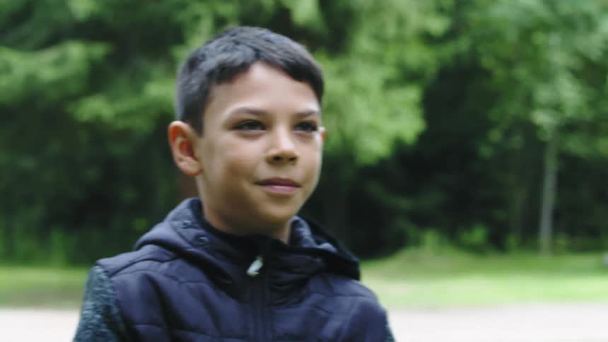 Boy standing across road from woods throws frisbee then smiles and jumps