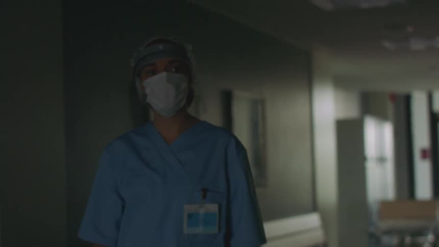Female nurse wearing scrubs face mask and face shield enters hospital via glass double doors