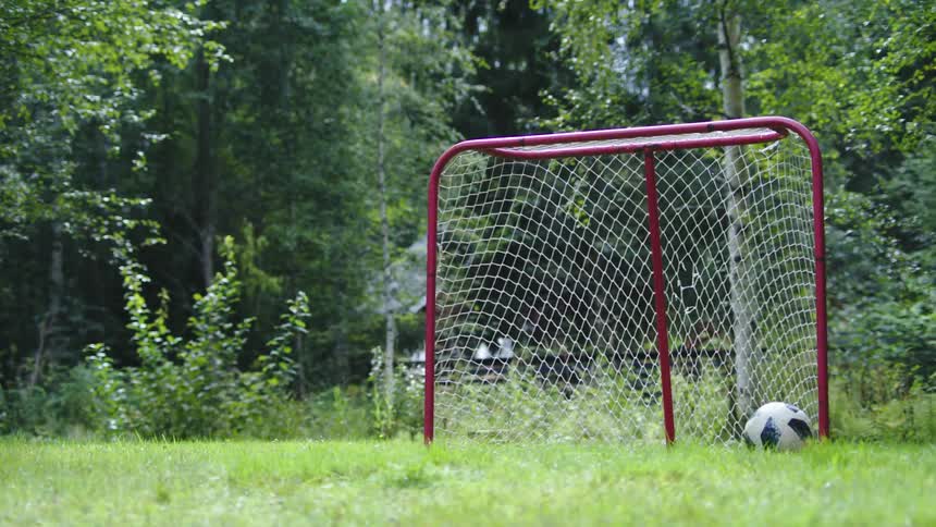 A soccer ball bounces across the grass and into the goal