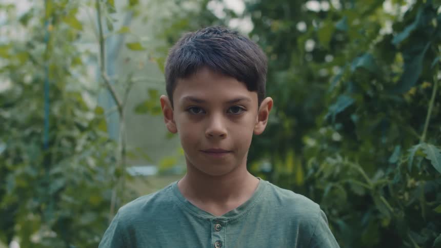 A boy is standing outdoors next to plants