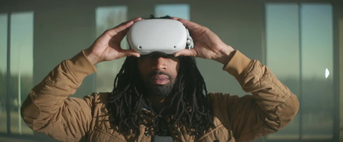A man stands in a building and puts on virtual reality goggles and then lifts them off as vehicles drive by on the street behind him