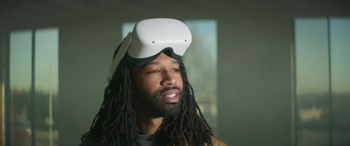 A man lifts virtual reality goggles off of his face as vehicles drive by outside