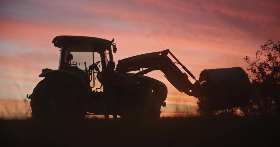 A person is getting out of a tractor at dusk