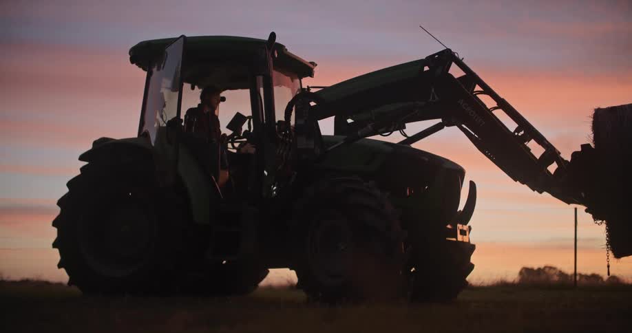 A man sits in a tractor in a field and types on a tablet