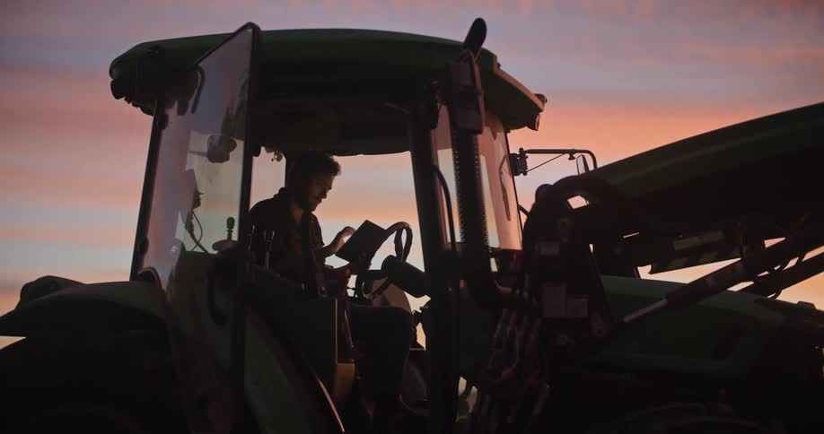 A man sits in a tractor and types on a tablet
