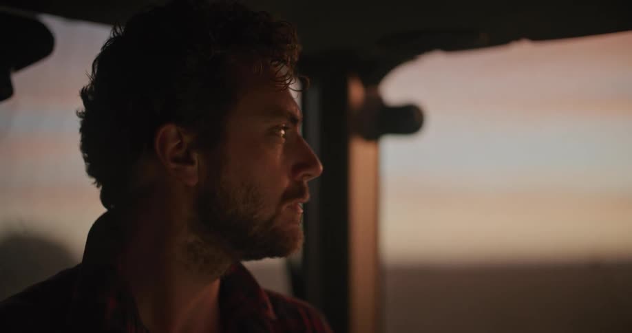 A man using a tablet as he sits in a tractor on a farm at sunset