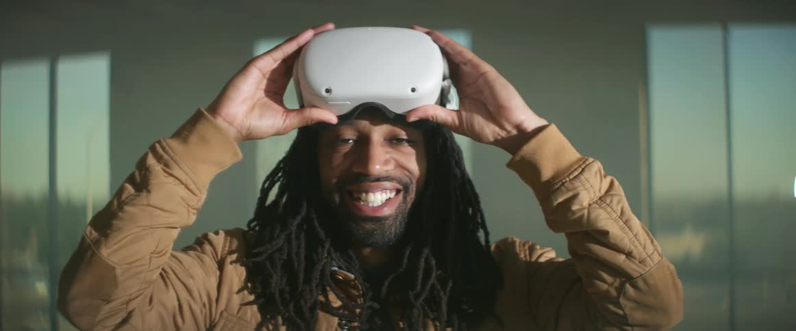 A man lifts virtual reality goggles off his face and smiles as cars drive by on the city street out the window