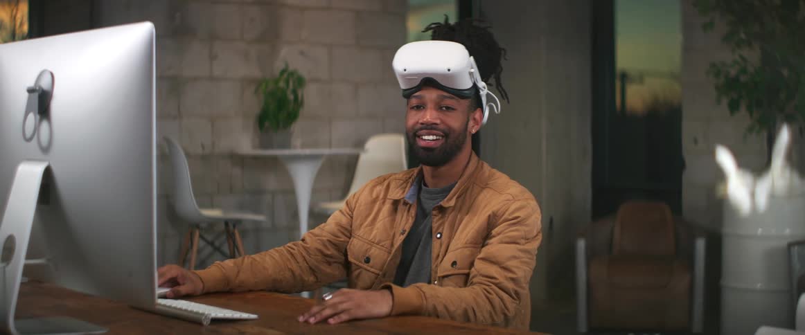 A man wearing a virtual reality headset sits at his computer