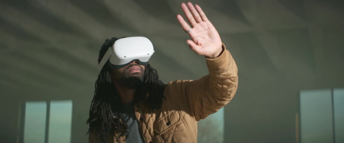 A black man is wearing a virtual reality headset and holding out his hand as he plays a game