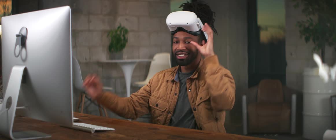 Man with braids and brown jacket takes off virtual reality headset smiling at camera and putting them back on