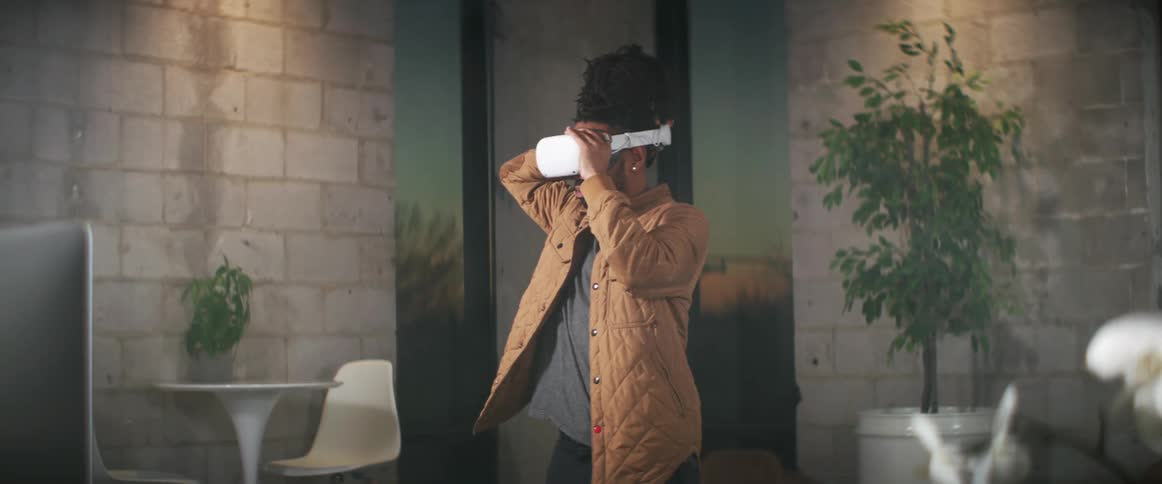 Man with braids brown jacket wears virtual reality headset smiling