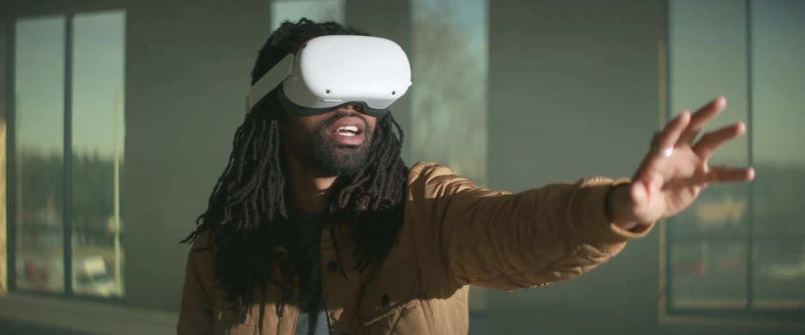Man with braids and brown jacket wears virtual reality headset moving his hands