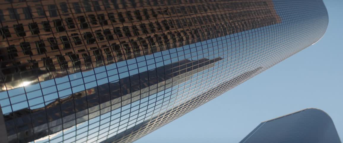 The glass facade of a skyscraper reflects the buildings surrounding it