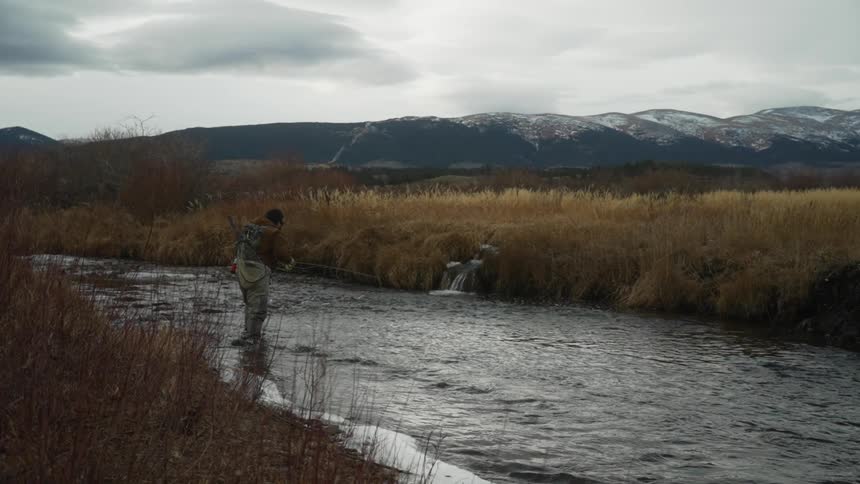 A man fishing in a river on a cloudy winter day