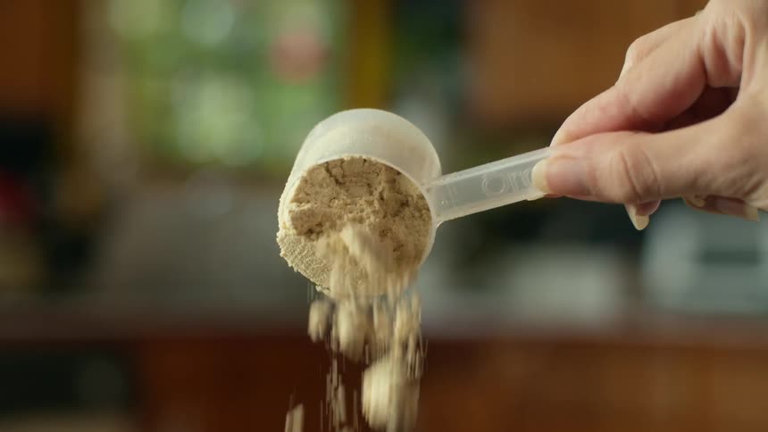 A woman pouring out a measuring cup full of brown sugar in a home kitchen