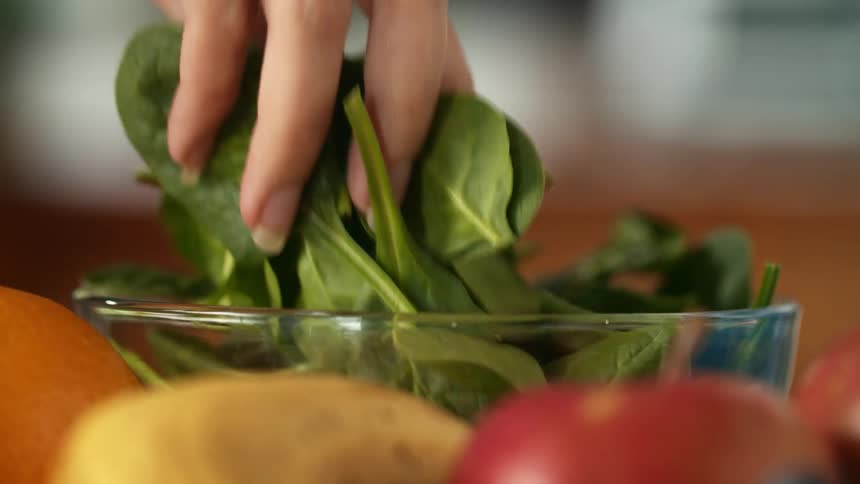 Womans hand with ring takes handful of spinach leaves from bowl in the kitchen