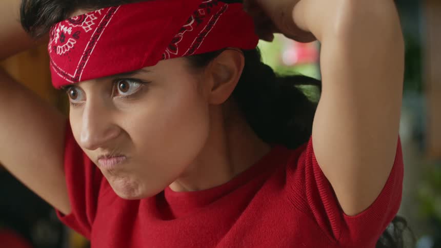 A teenage girl is making a mean face and putting a red bandana on her head