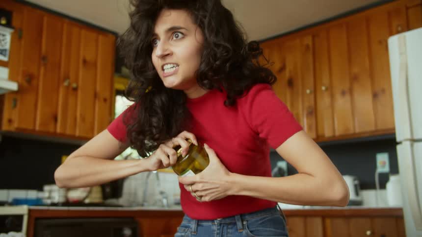 A teenage girl struggles to open a jar of pickles and then slaps herself in the face and tries again
