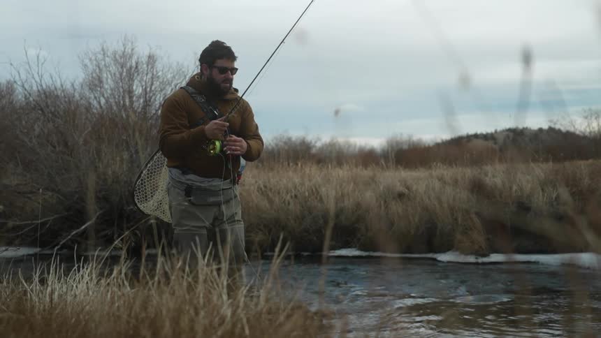 A fisherman is standing on a river bank holding his pole