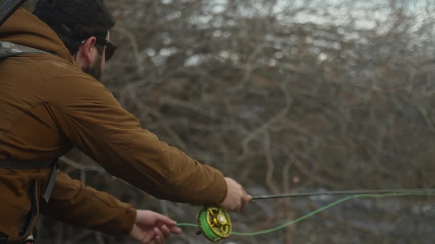 A man casting a fishing line into a river on a cold winter day