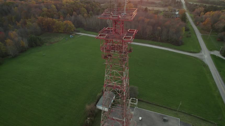 A utility tower is high above trees and grass below