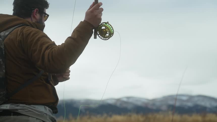 A fisherman is standing on a river bank and casting his line