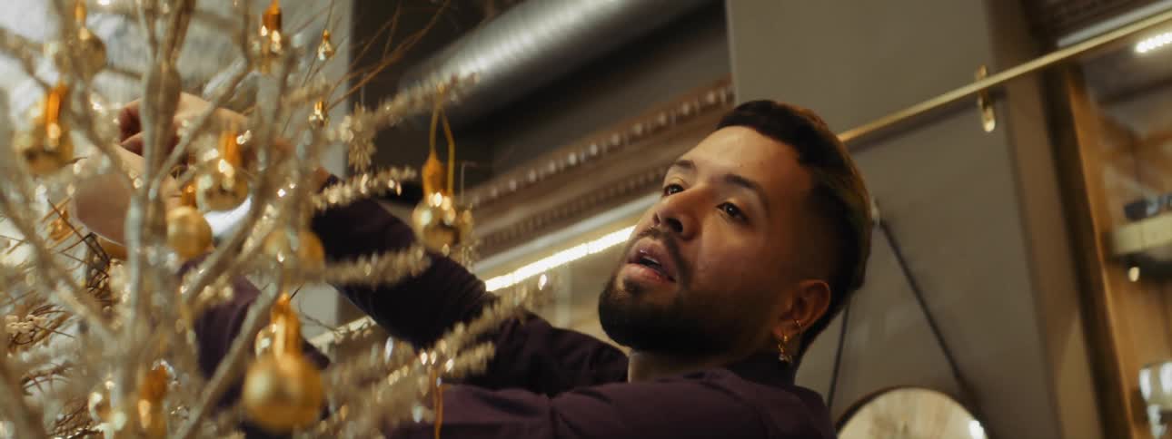 Man with beard and earrings attaches decorations to golden tree