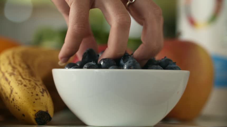 A woman taking a handful of blueberries from a white ceramic bowl