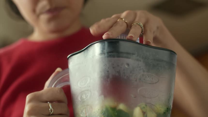 A woman putting a lid on a blender full of fruits and vegetables