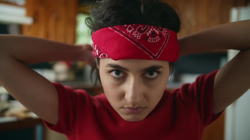 A teenage girl is putting a red bandana on her head and tying it
