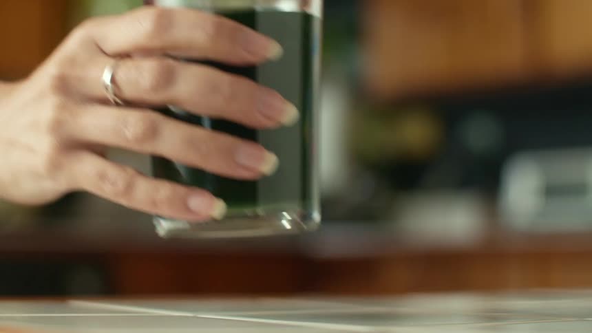 A woman with long fingernails picking up a glass with beverage from a kitchen counter