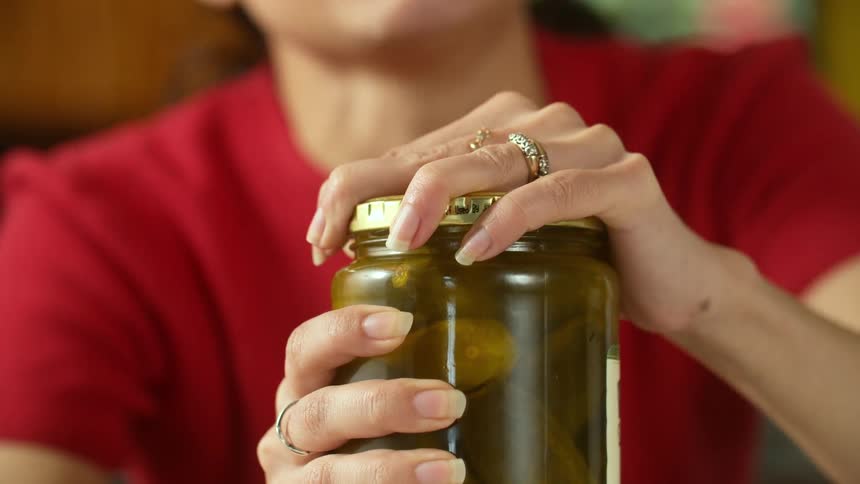 A young woman making funny faces while struggling to open a pickle jar
