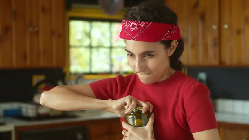 A woman is in her kitchen and opening a jar of food