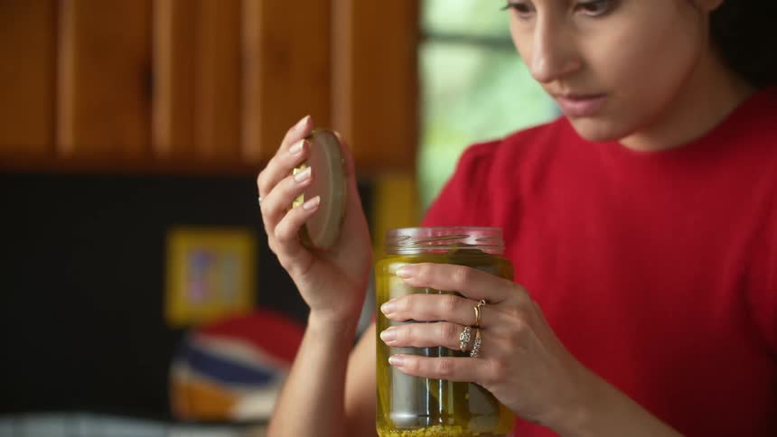 A woman is opening a jar of pickles