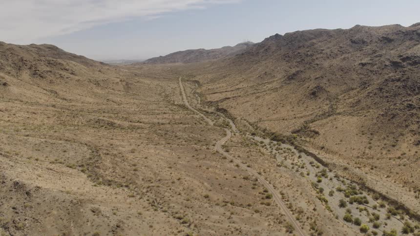 Road stretches through arid scrub filled valley paralleling arroyo