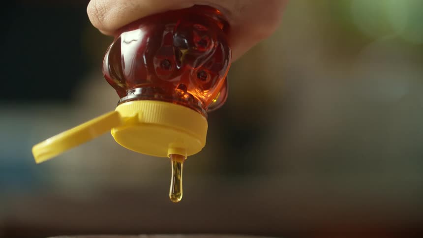 A person squeezing a bear bottle of honey