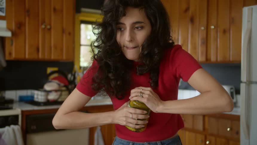 A woman is trying to open a jar of pickels