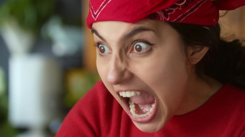 A woman with a red bandana opening her mouth and making an angry face