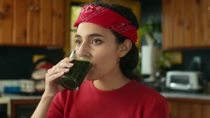 A young woman hesitantly drinking a smoothie in a home kitchen