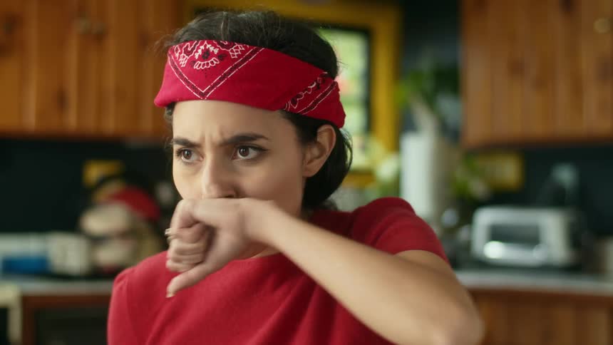A woman making a face and wiping her mouth after drinking a smoothie in a home kitchen
