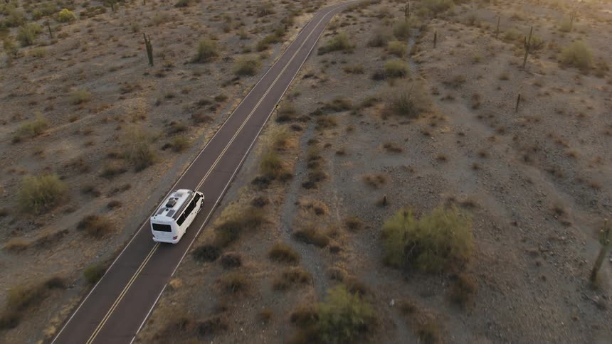 Aerial view of white van driving on highway at sunset in desert
