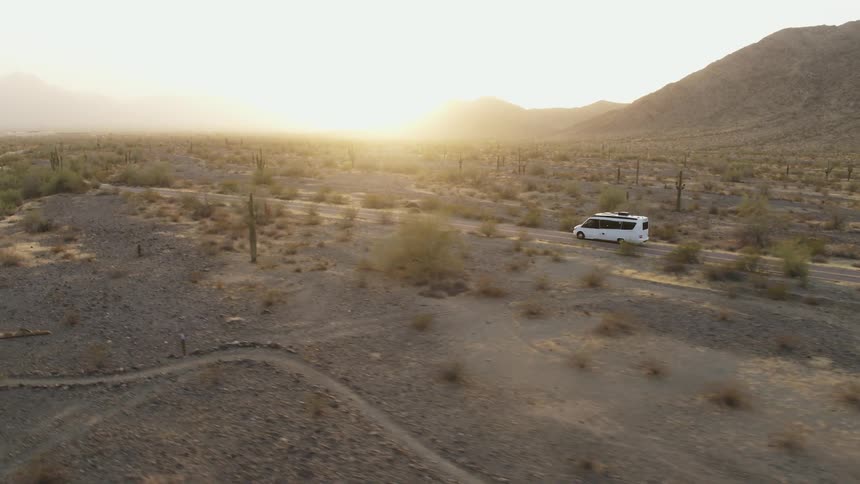 A white van traveling on a remote desert road at sunrise