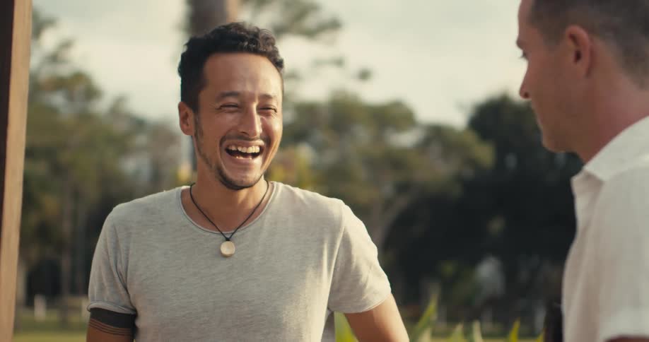 A man laughs while talking with another man outdoors during the day