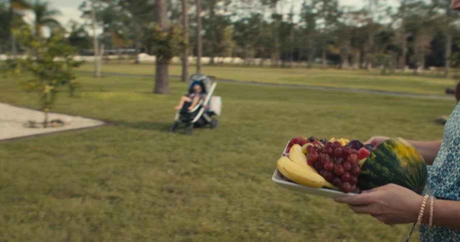 A woman carries a tray of fruit through a park