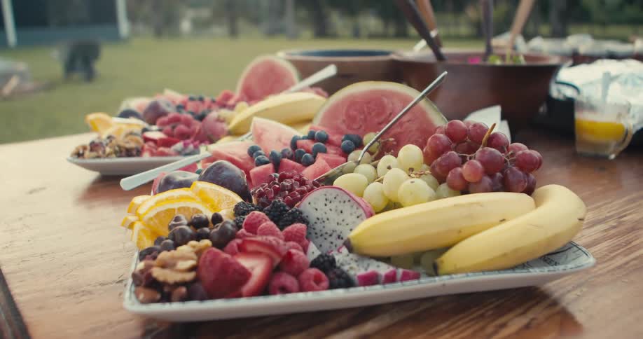 Fruits and salad sit on a picnic table near a campfire