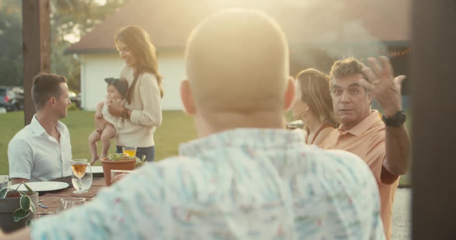 A group of friends sitting at table drinking alcohol has barbecue in the garden at dusk