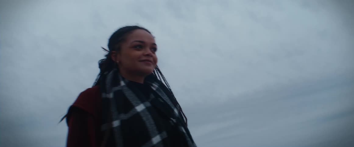 A woman wearing a poncho is standing on a mound along the coast